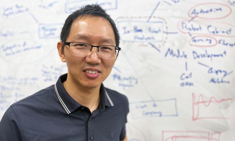 Yue Chen stands in front of a white board with a variety of writing and diagrams.