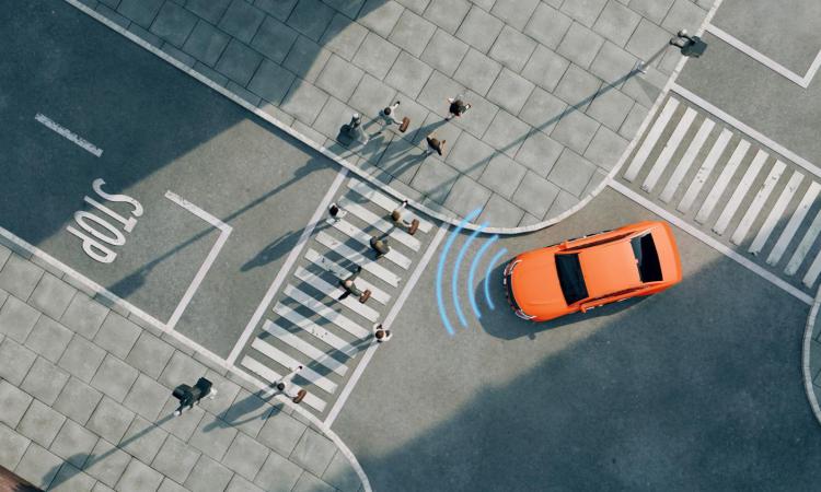 Overhead view of an orange car turning in an intersection toward a crosswalk full of pedestrians. A series of curved blue lines at the front of the car indicate it sensing those walkers.