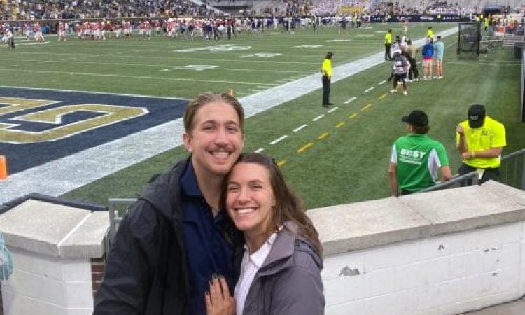 Michael Bauby and his girlfriend pose in the stands at Bobby Dodd Stadium with the field behind them.