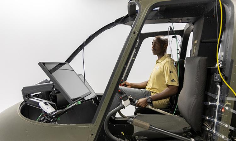Side view of a male student operating a helicopter simulator with no front windows.