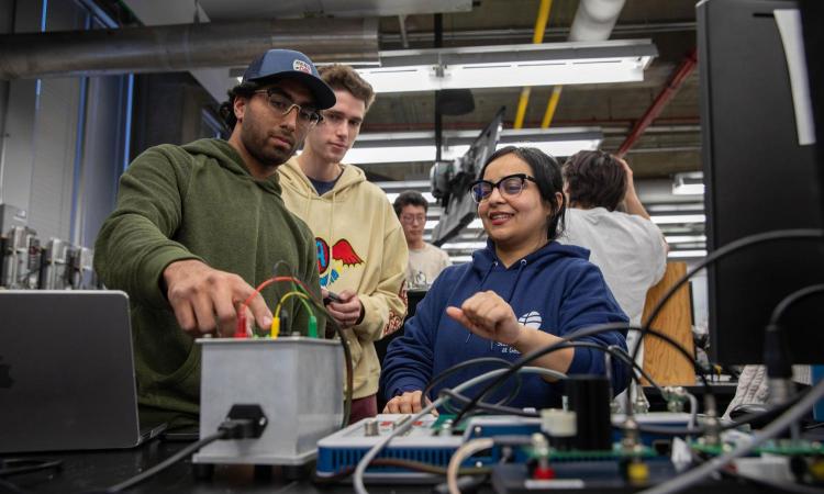 Students and a faculty member standing in the background look at equipment on a table in the foreground in ME 3057, Experimental Methods.