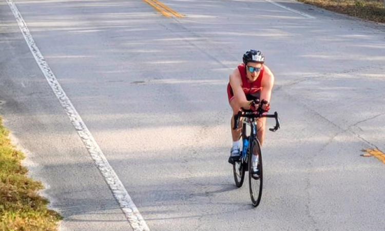 Jacob Beldick riding a bike on a two-land road during the biking portion of the Ultraman Florida triathlon.