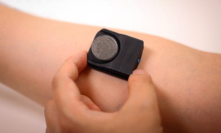 A hand holding a black rectangular device against the skin of an arm.