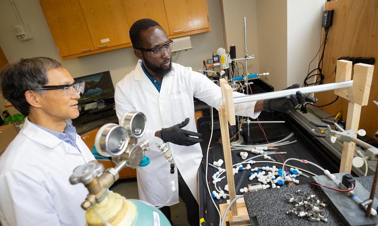 two people work with a wastewater reactor system in a lab