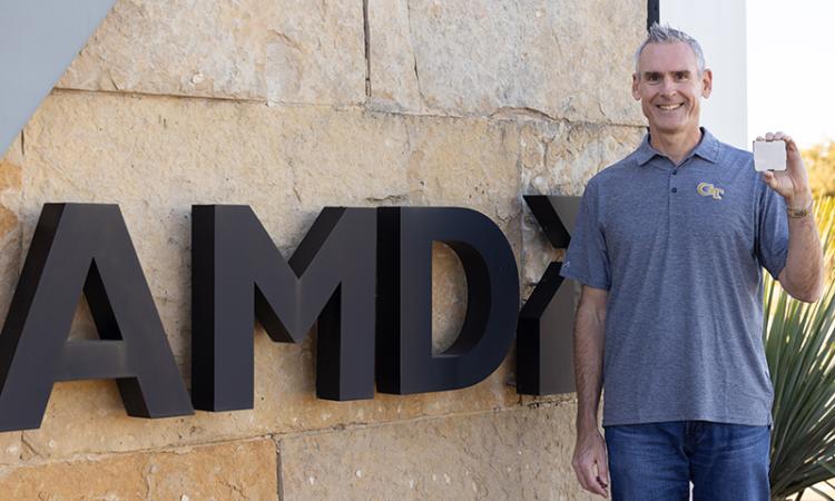 Alan Smith holds a computer chip while standing next to an AMD sign.