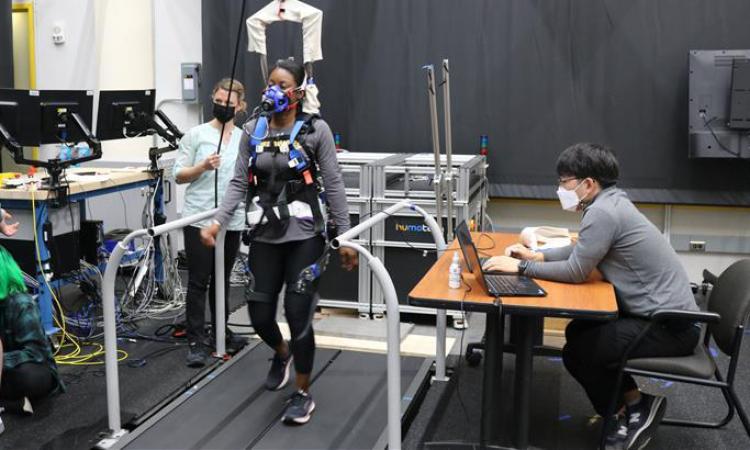 A test subject wearing a robotic exoskeleton walks on a treadmill in a research lab.