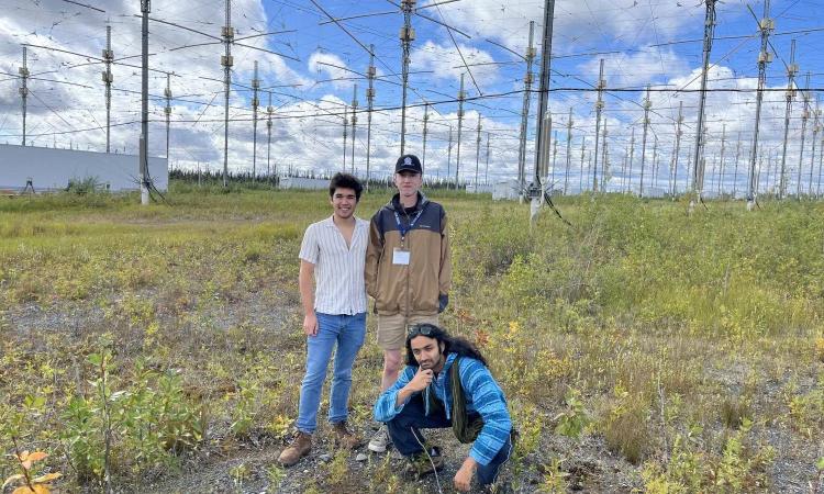 Three students pose in front of a field of antennas that are part of the Ionospheric Research Instrument in Alaska.