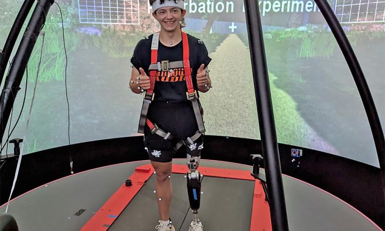 A student with a prosthetic leg stands on a walking device in the lab