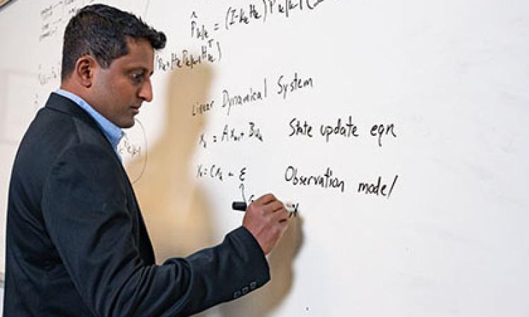 Chethan Pandarinath writing formulas on a whiteboard.