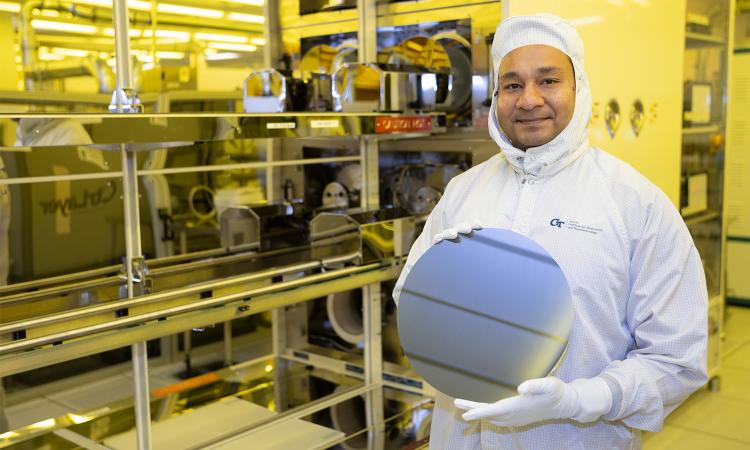 a man in a cleanroom suit holds a silicon wafer computer chip