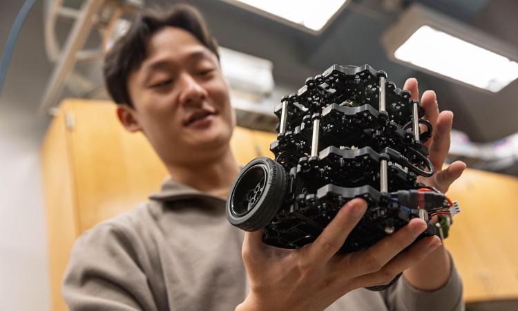 A researcher holds a small mobile robot in his hands.