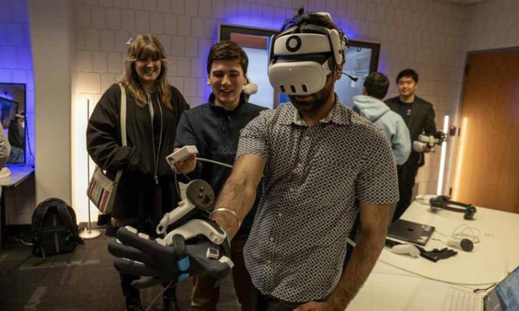 Students test a headset and haptic glove at the opening of the new XR Makerspace.