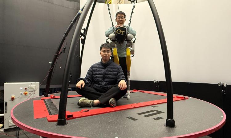 Yipu Chen and Zhaoyuan Gu stand on a moving treadmill platform with their two-legged robot.