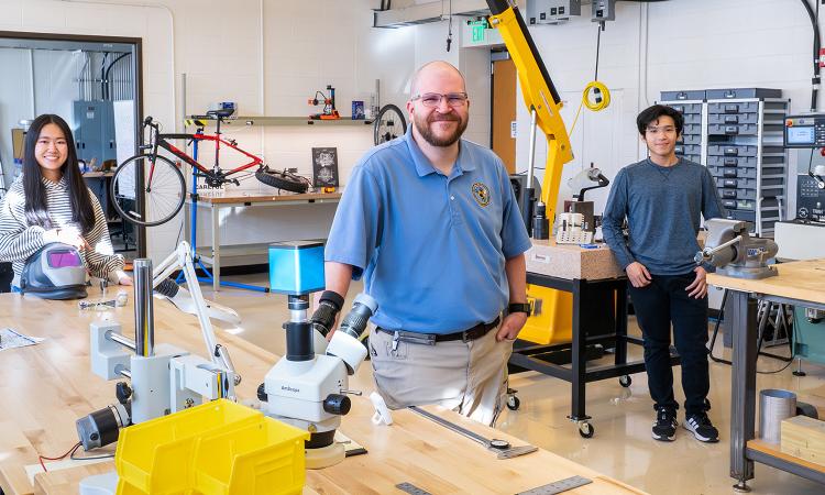 three people in a mechanical shop with tools and workbenches