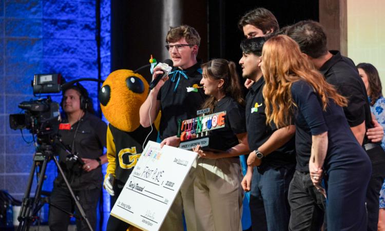 A group of students speak to the audience while holding a first-place trophy and winners check