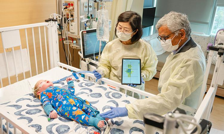 two researchers in gowns and masks observe a hospitalized infant lying on sensor fabric