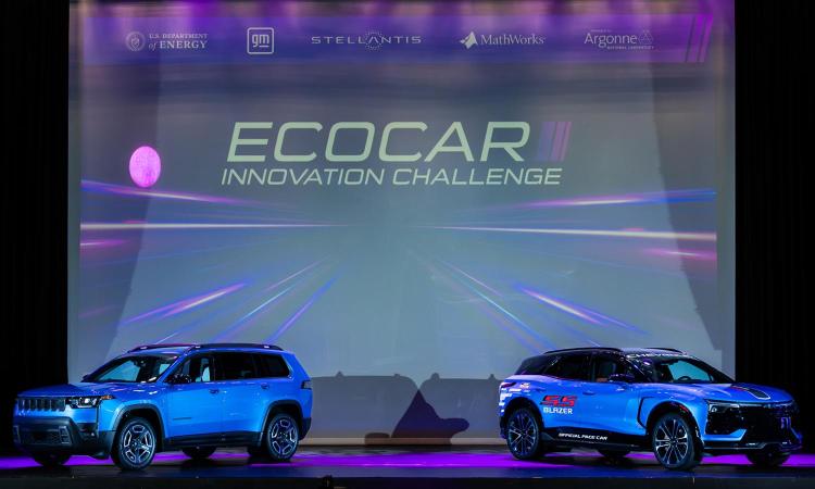 Two vehicles on a stage in front of a screen with text, "EcoCAR Innovation Challenge."