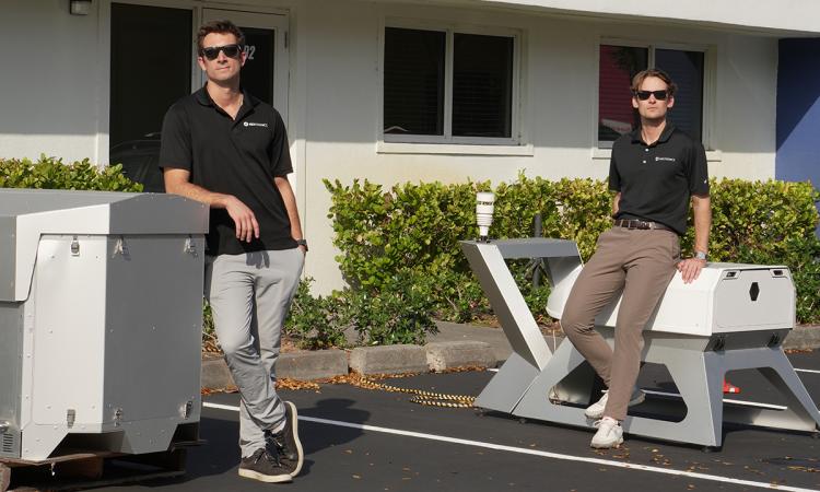 two people stand outdoors with drone docking stations