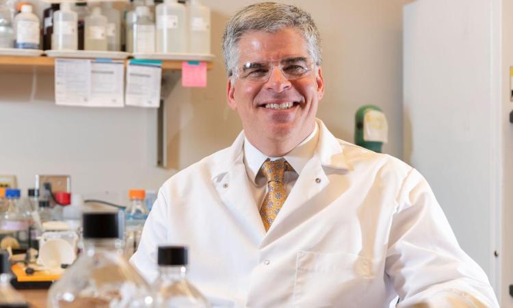 Andres Garcia smiling at camera while inside, wearing a white lab coat
