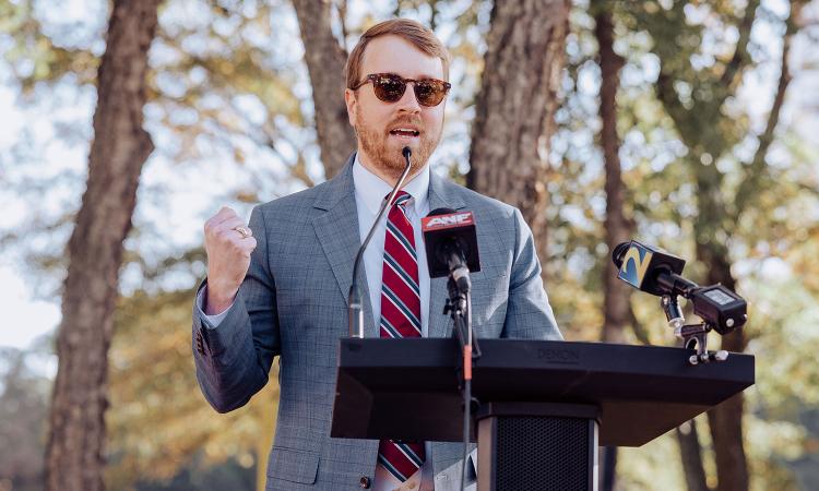 Jack Cebe speaks at a podium with news microphones