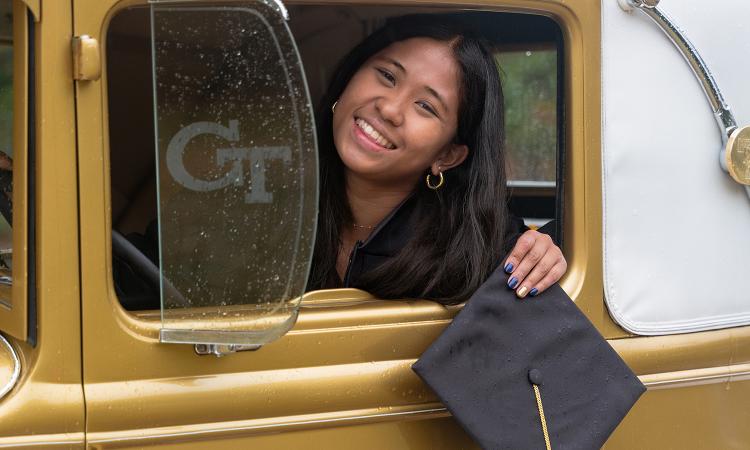 Tiana Fontejon sits in the Ramblin' Wreck and holds her graduation cap out of the window.