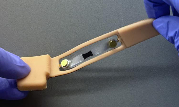 Two gloved hands twist a skin-like nasal patch with flexible electronics.