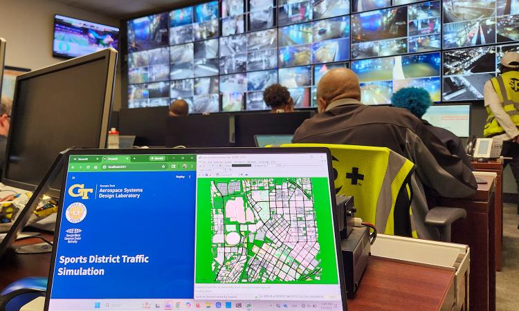 a laptop screen in the foreground shows a map of Atlanta, with a wall of camera feeds in the background