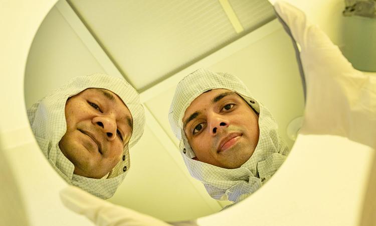 Asif Khan and Lance Fernandes reflected in a round semiconductor wafer in the Georgia Tech cleanroom.