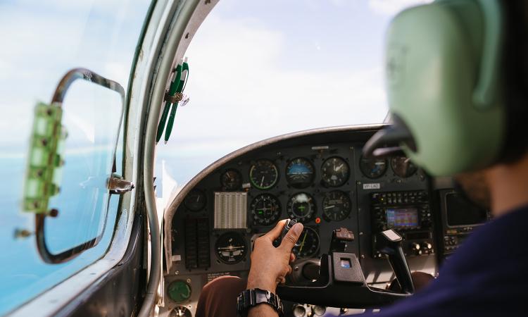 View of a small plane cockpit from behind the pilot's left shoulder.