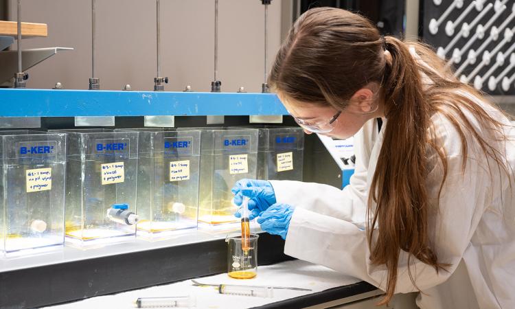 A woman uses a syringe to manipulate liquid in a beaker.