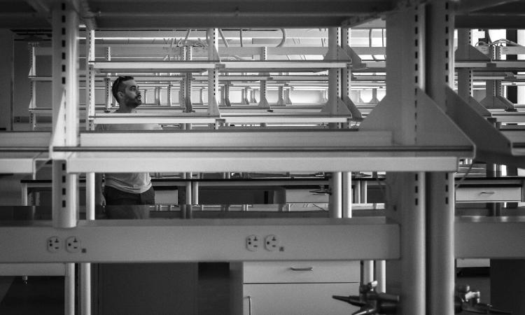 Alexander Vlahos seen through rows of empty lab shelves.