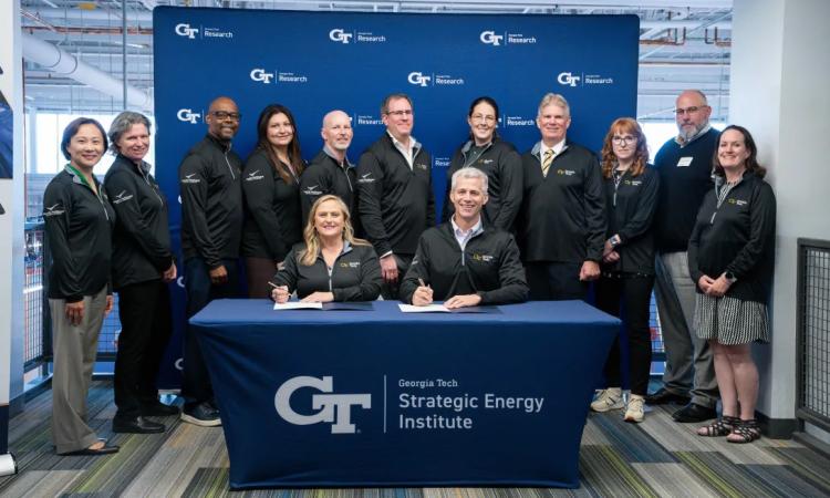 A group of people pose around a table where two leaders are signing a memorandum of understanding.