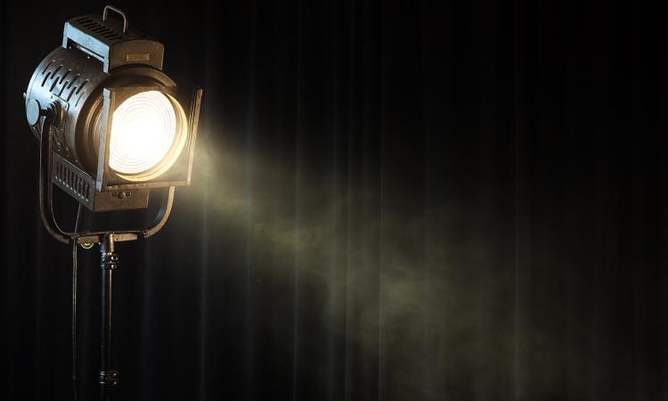 Vintage theatre spotlight shines on wisps of smoke in front of a black curtain