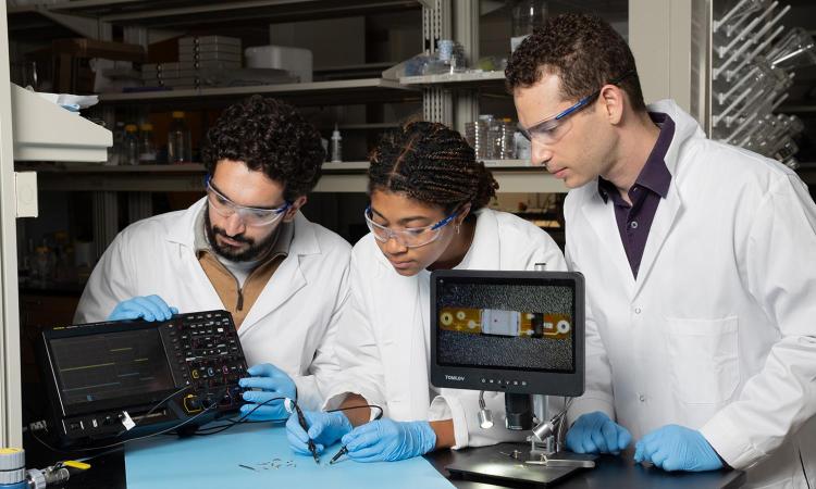 Three researchers test a tiny implantable device in the lab.