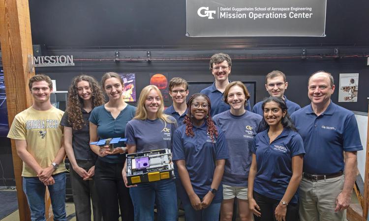 Student controllers pose with a model of the GPDM CubeSat in the Georgia Tech Mission Operations Center.