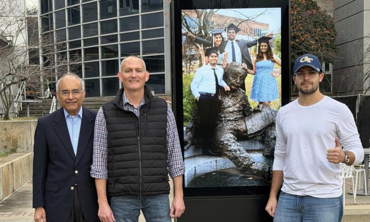 Three researchers and company representatives pose with one of MRI's outdoor digital displays on the Georgia Tech campus.