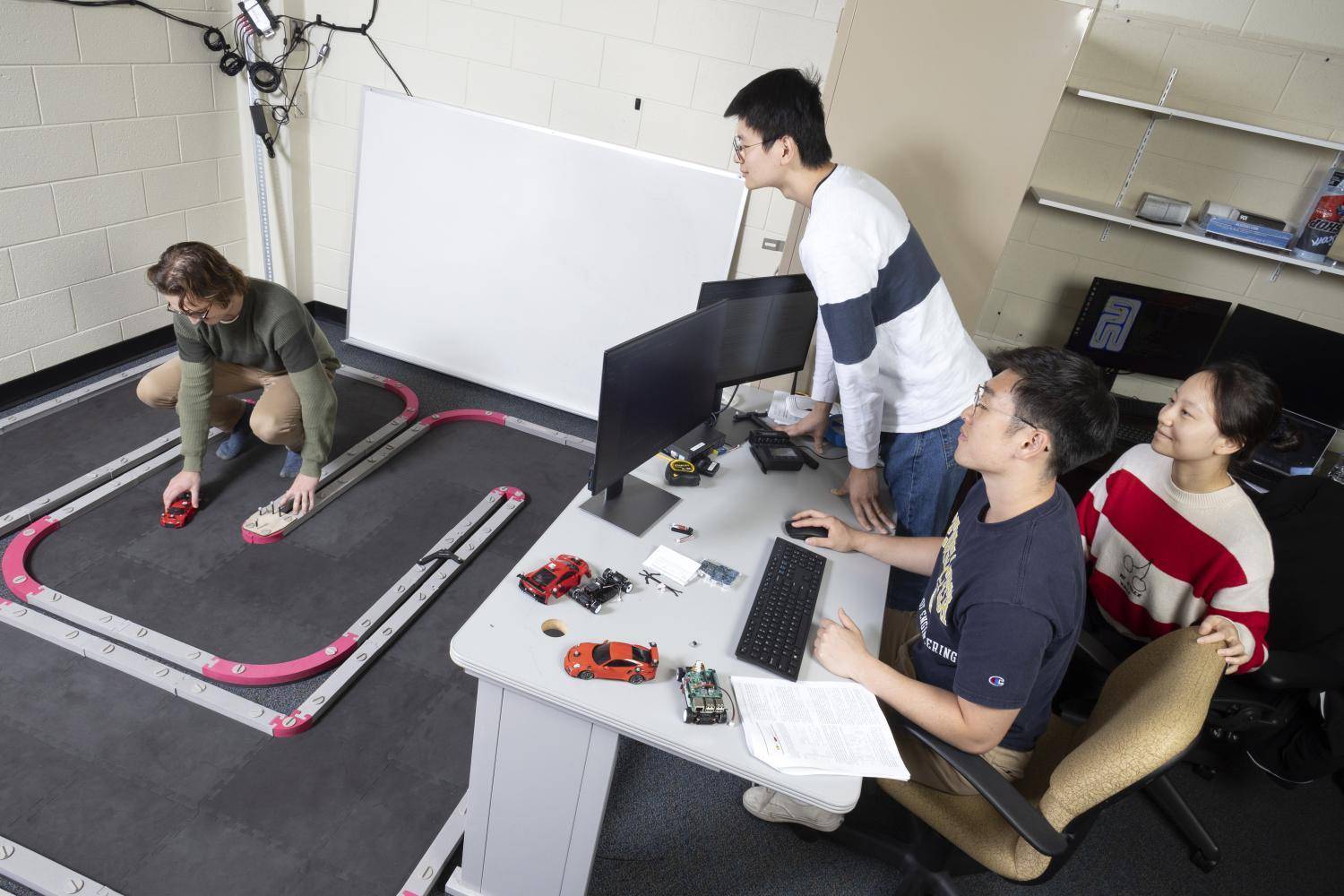 A team of students works with scale model cars on a track to simulate driving scenarios