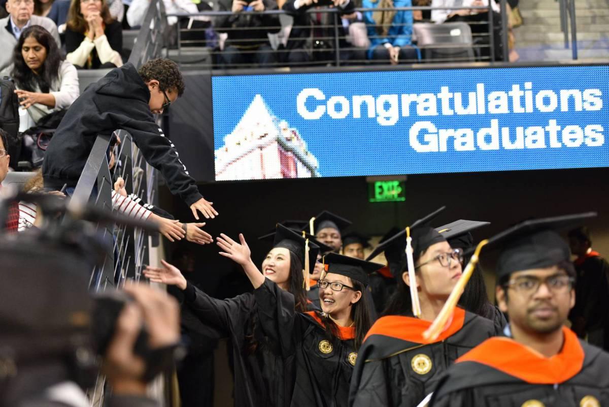 A student reaching to a child during graduation ceremonies.