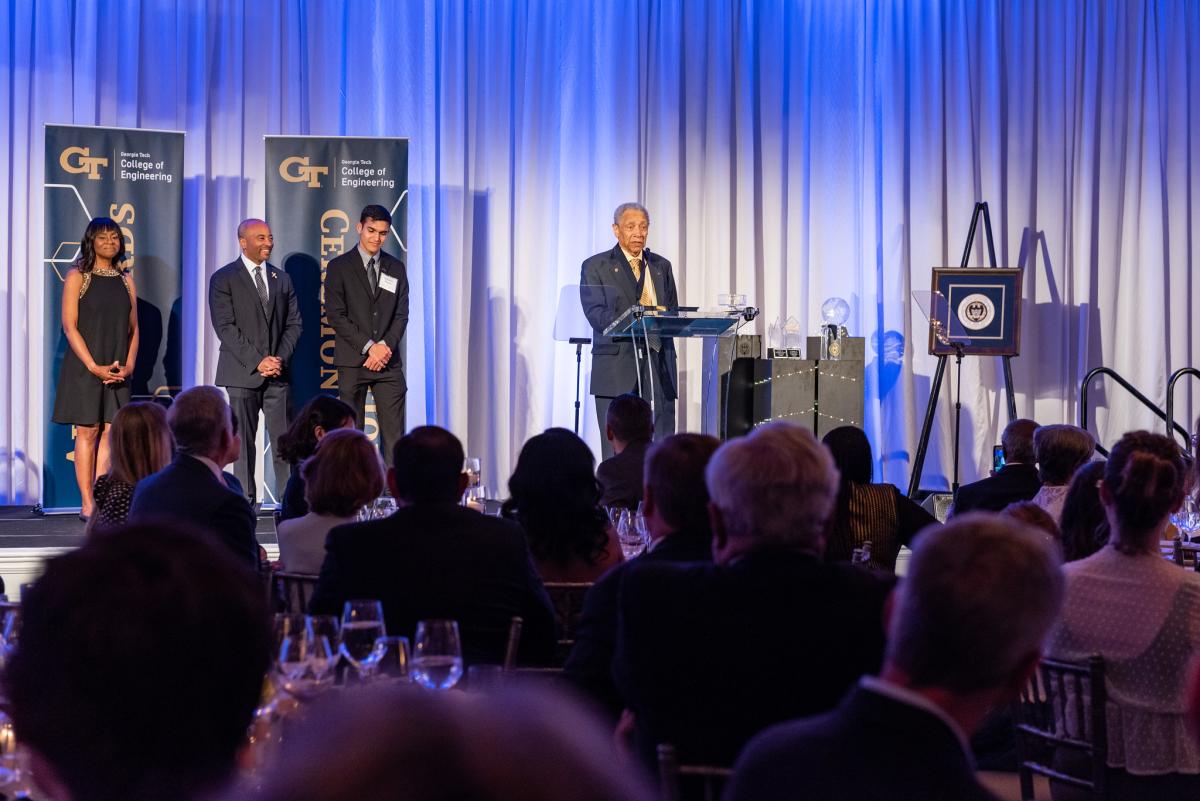 Person standing at podium with three others on stage