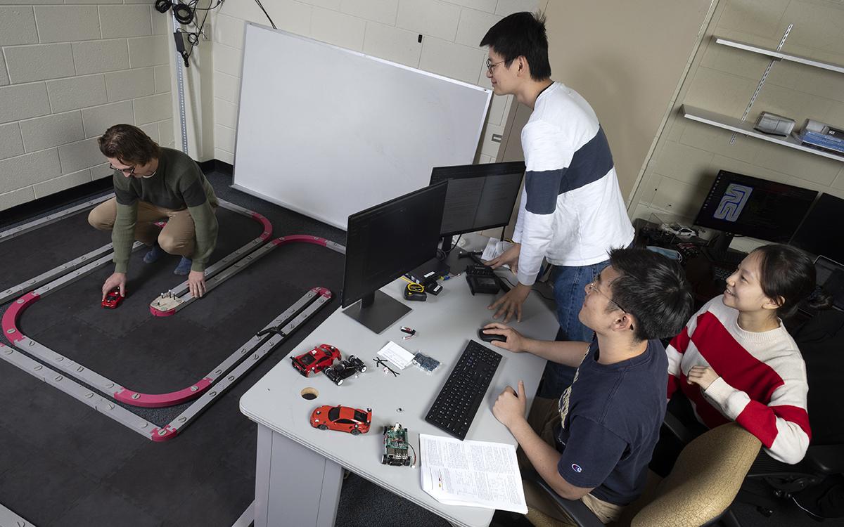 A team of students works with scale model cars on a track to simulate driving scenarios