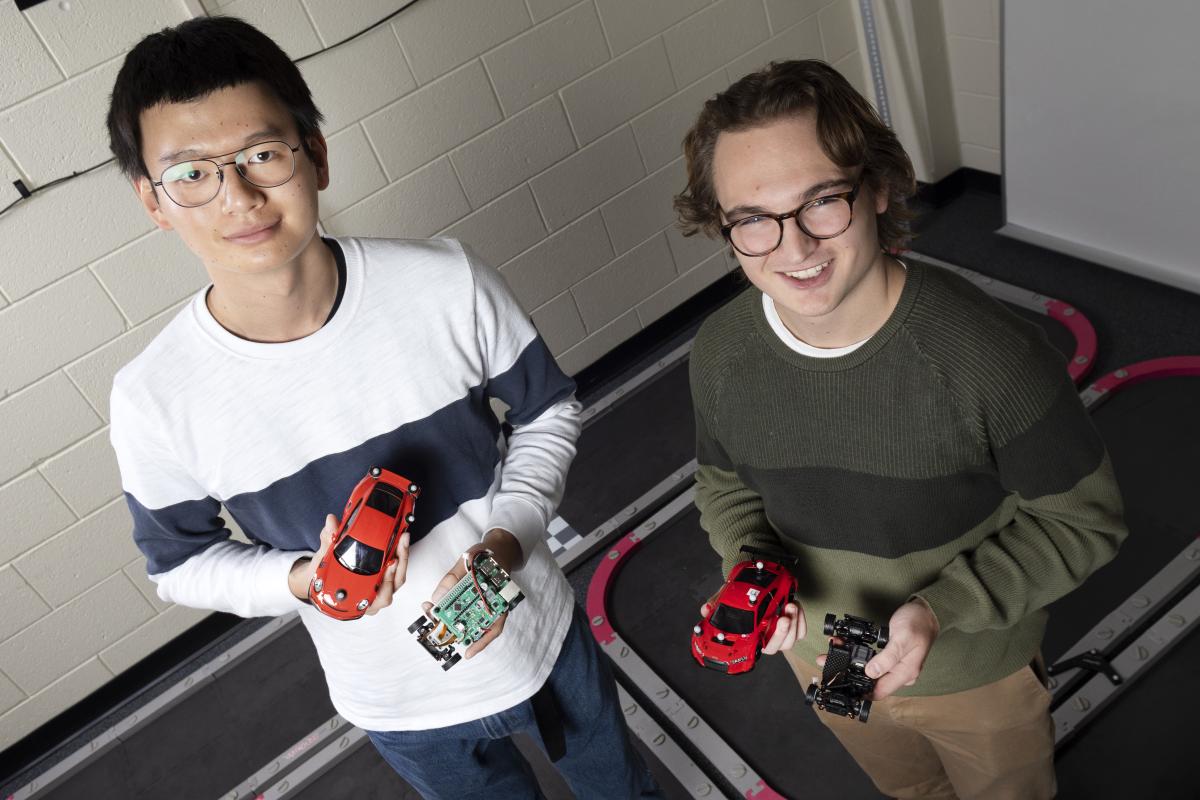 Two VIP students display scale model cars with a test track in the background