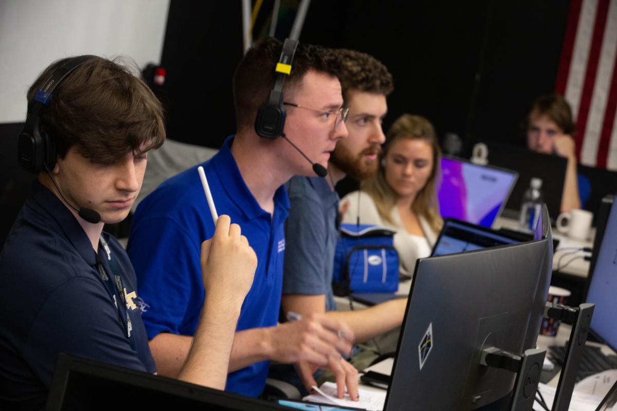 Conner Awald, Mason Starr, and Michael Hauge sit at their computer screens in mission control with headsets on during a readiness test.