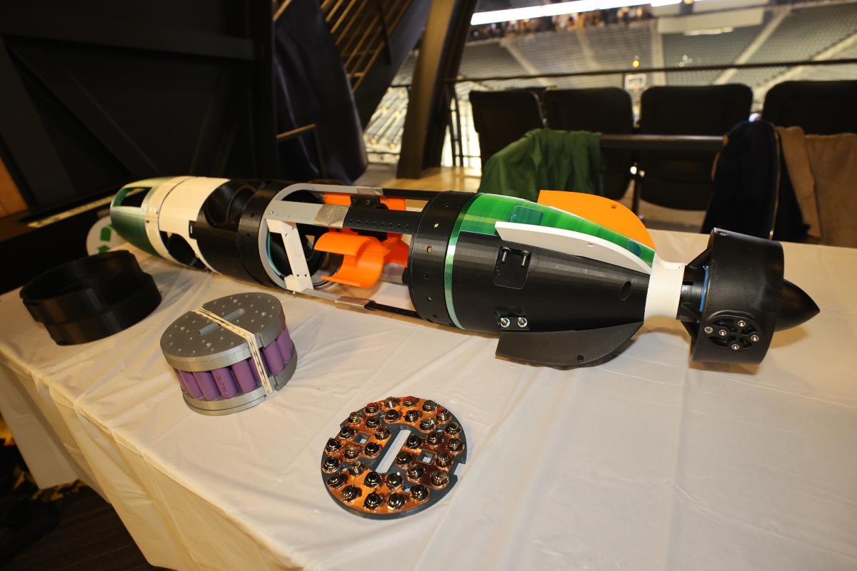 An underwater autonomous vehicle shaped like a torpedo on a table. Side plating is removed from the fuselage allowing a view to the inside mechanical components.
