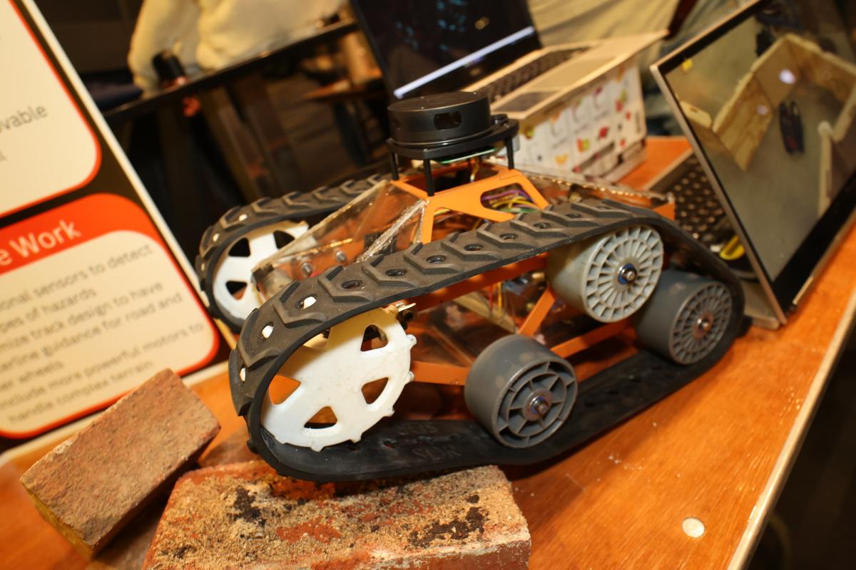 A small vehicle with treads rolling over bricks on a table.