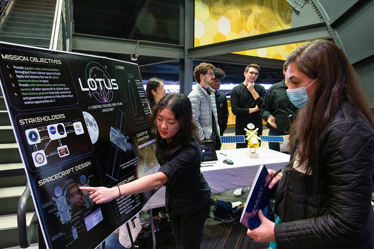 two people look at the poster for the LOTUS capstone team, with other people in the background