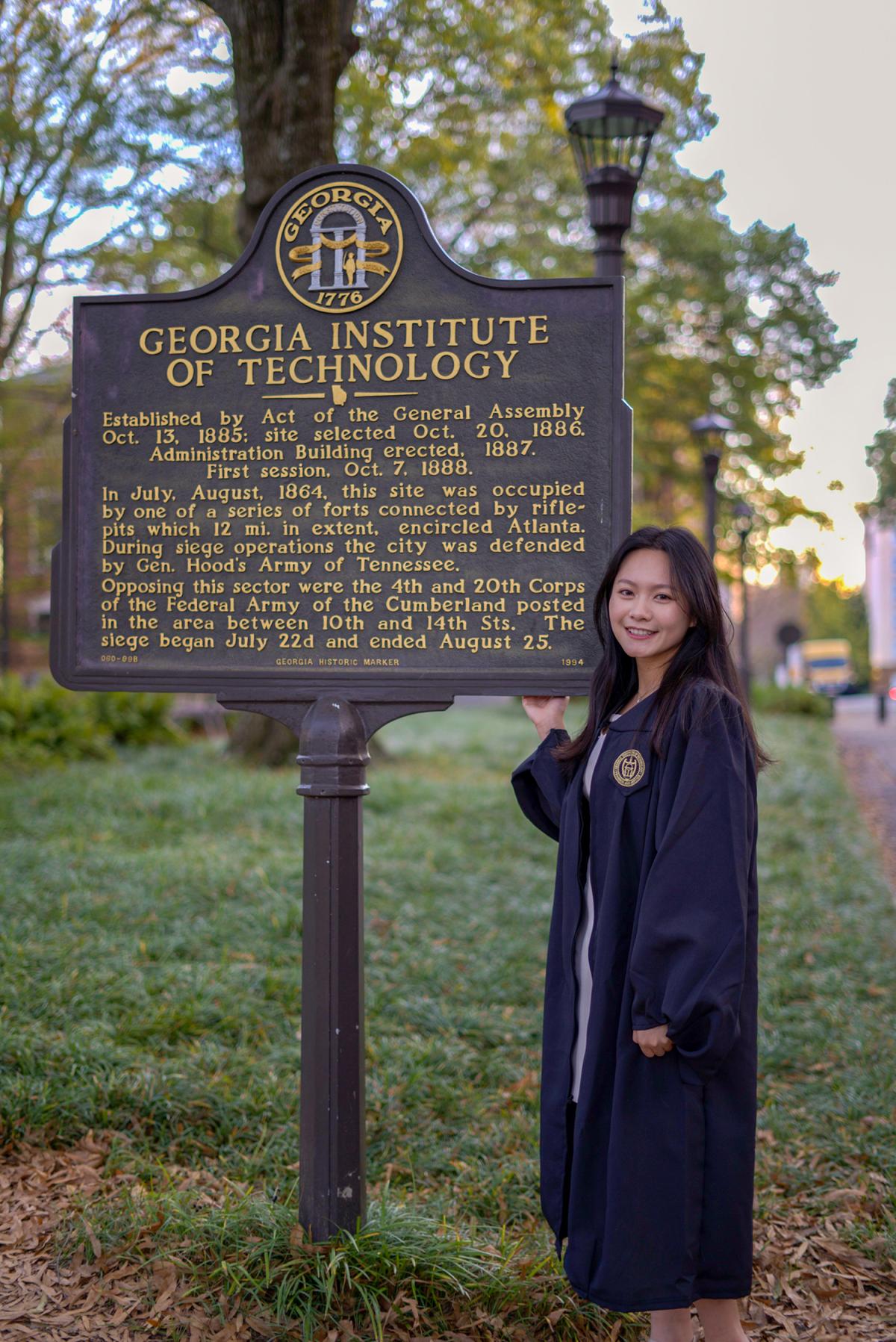 Victoria Lynn in commencement regalia next to the Georgia Tech marker