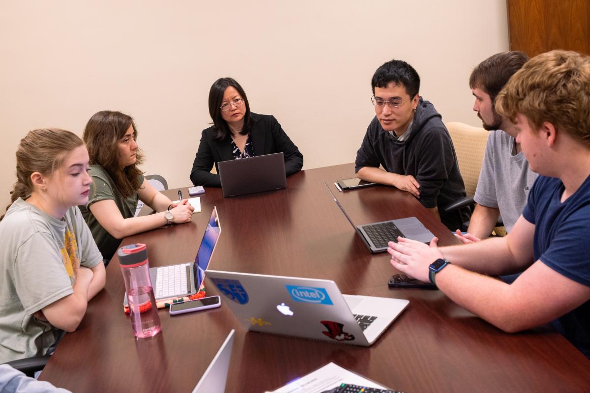 Ying Zhang works with a group of students at a conference table