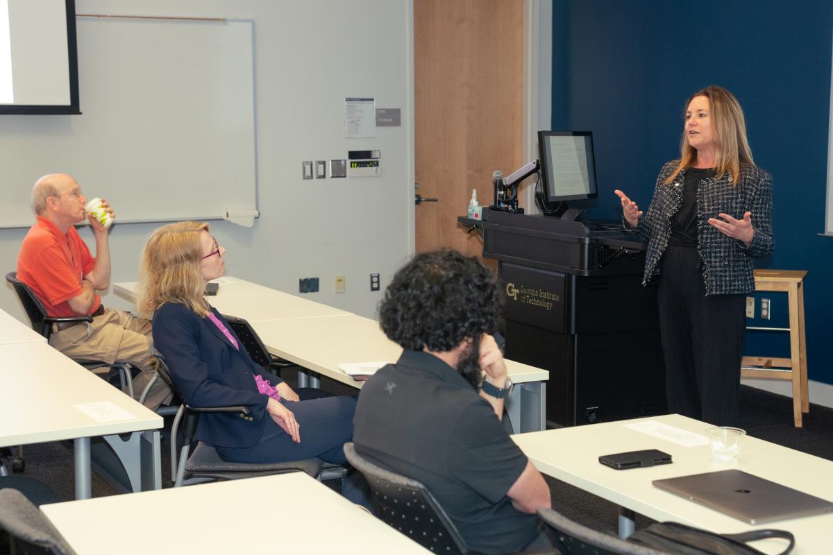Kim Kurtis lectures at the front of a classroom with three people in the audience