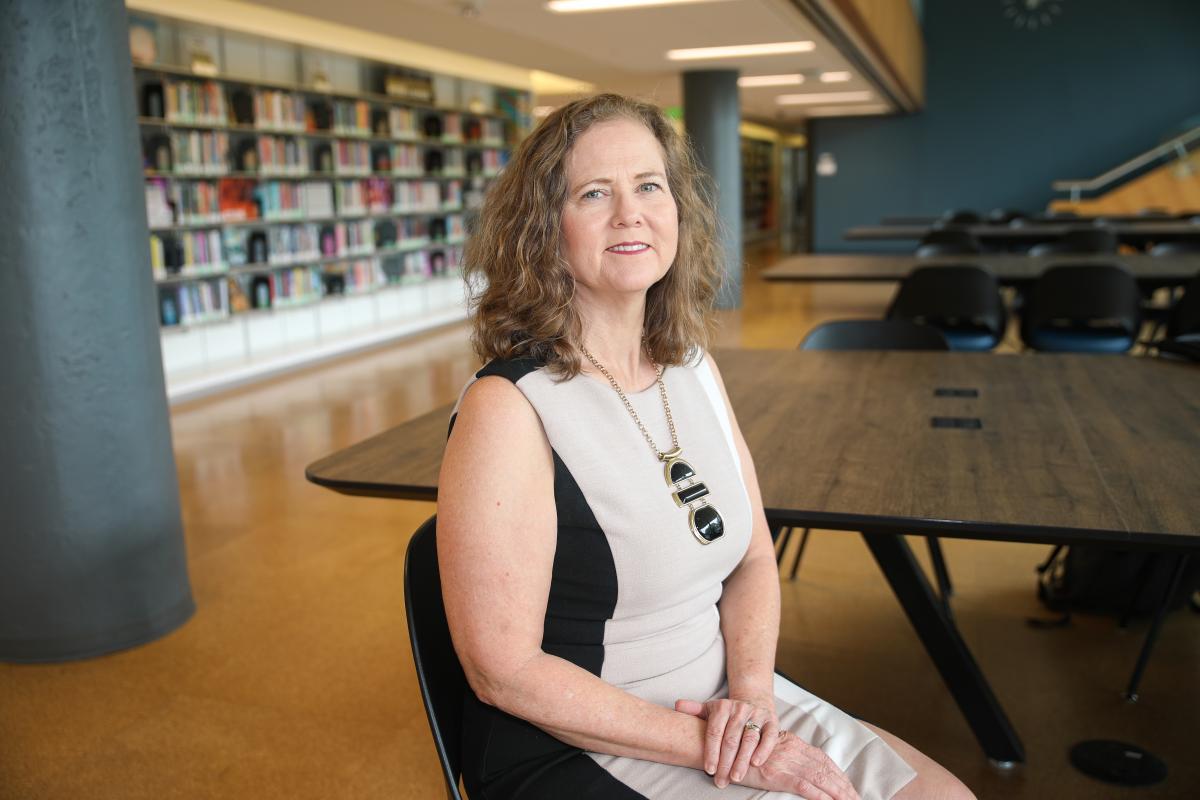 Mary Lynn Realff seated at a table in the library with bookshelves in the background