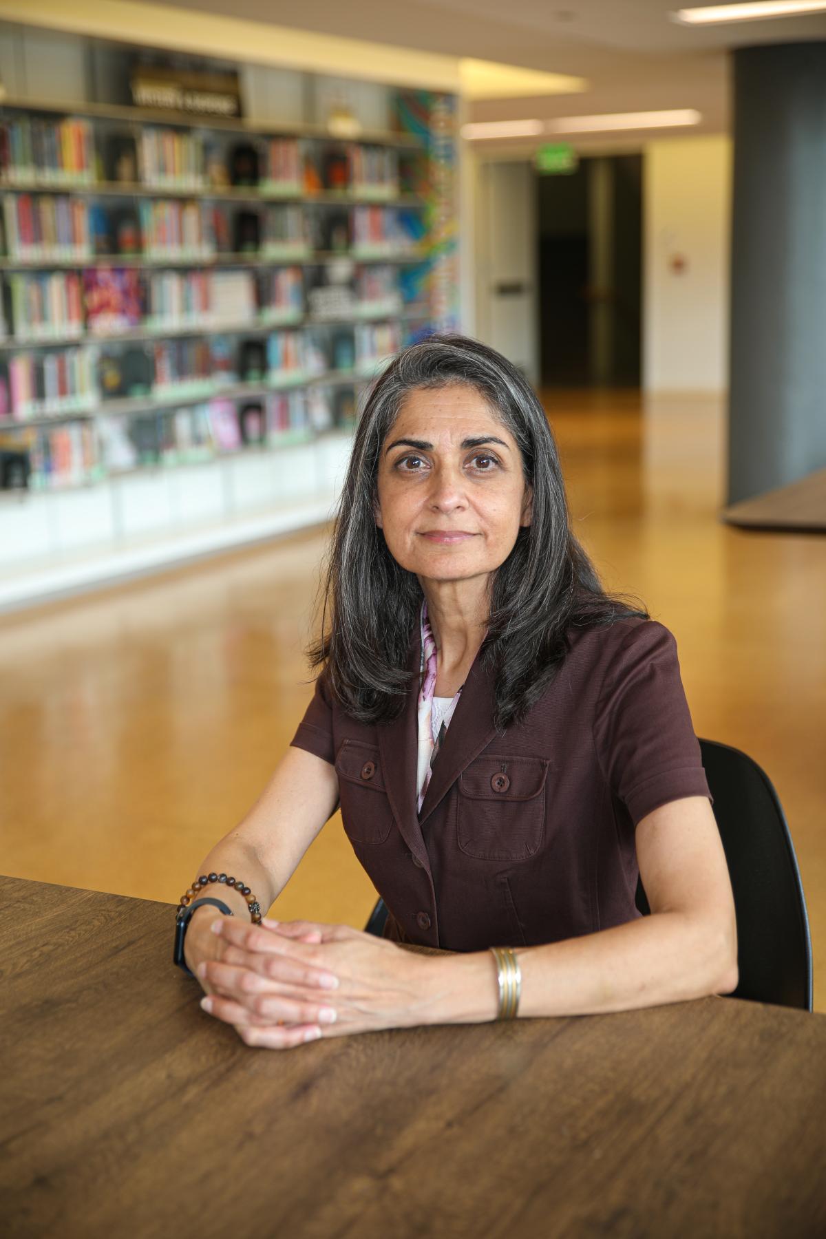 Pamela Bhatti seated at a table in the library with bookshelves in the background